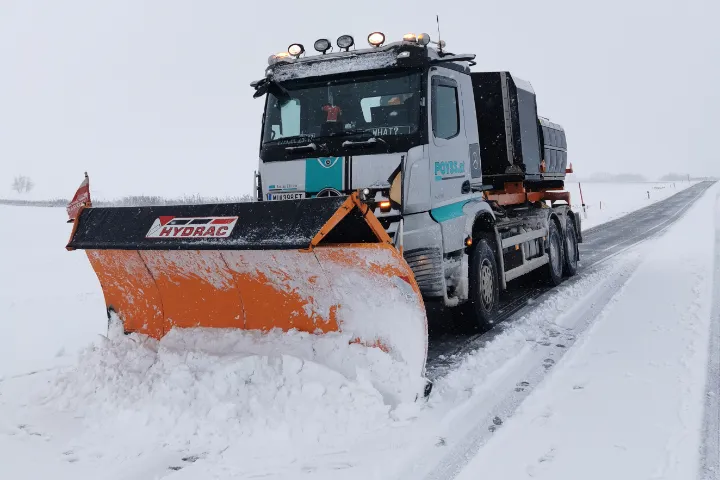 LKW mit Schneepflug im Winterdienst auf verschneiter Straße